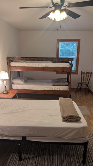 A bunk bed room with a ceiling fan, a window with blinds, a lamp, and a chair.