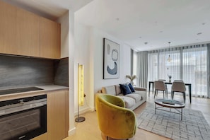 A modern kitchen with a built-in oven and a dining area with a table and chairs. - Refined King’s Cross Apartment | StayCozy (London)