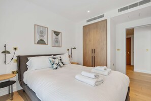 A modern bedroom with a large bed, two wall-mounted lamps, a wooden wardrobe, and two abstract wall art pieces. - Refined King’s Cross Apartment | StayCozy (London)