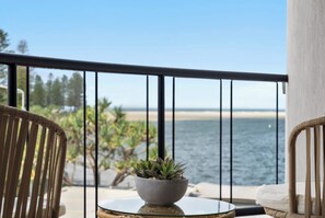 Een balkon met uitzicht op zee, een rond glazen tafeltje met een plant en rieten meubels.