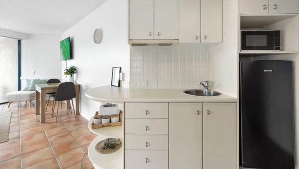 Eine moderne Küche mit weißen Schränken, einem schwarzen Kühlschrank und einem Essbereich mit Tisch und Stühlen.