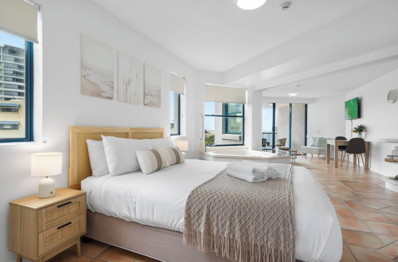 A modern hotel room with a large bed, bedside tables, a desk, and a view of the city.