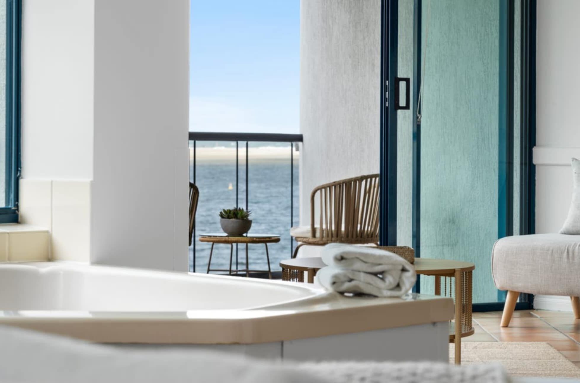 A modern bathroom with a bathtub, a small table with a plant, and a chair.