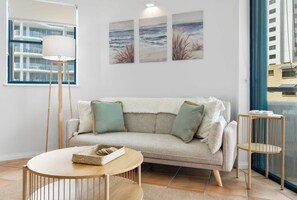 A living room with a sofa, a round coffee table, a floor lamp, and artwork on the wall. - La Promenade Unit 12 (Caloundra)