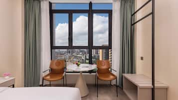 Une chambre d’hôtel avec une grande fenêtre, deux chaises, une petite table et un lit.