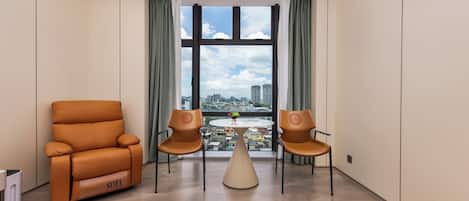 Habitación de hotel con sofá, dos sillones, una mesita y vistas a un paisaje urbano a través de amplios ventanales.