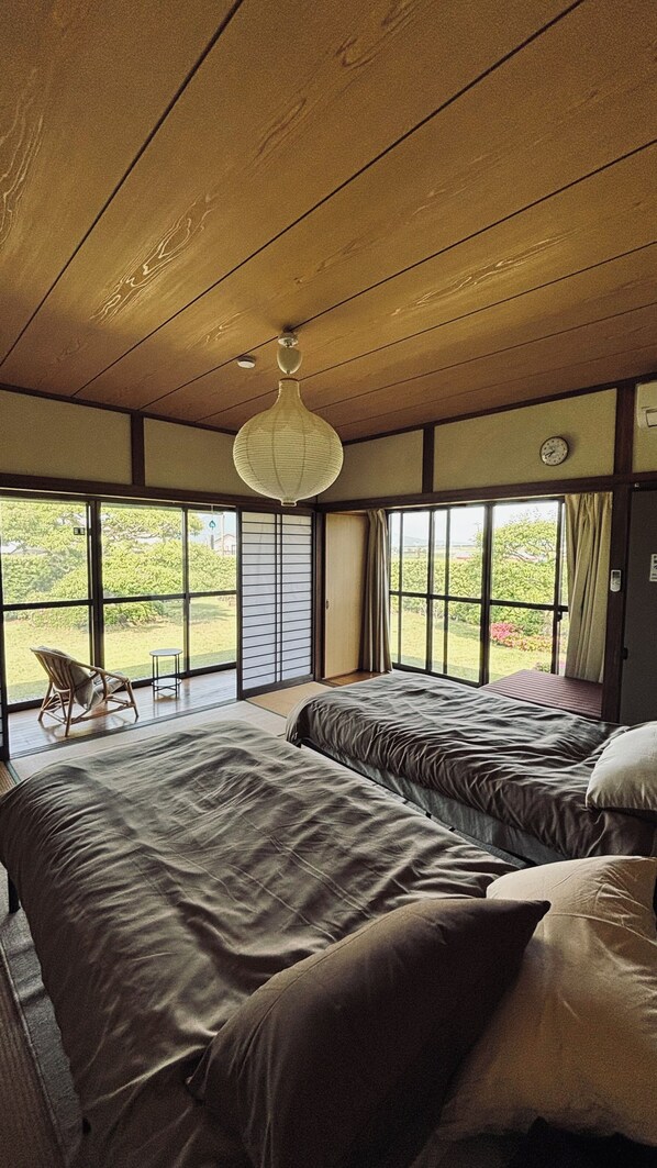 A room with two beds, a chair, and a view of greenery outside.