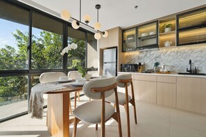 A modern kitchen with a large window, a dining area with a table and chairs, and a built-in oven. - Jasmine by Kozystay - Nusa Dua (Badung)