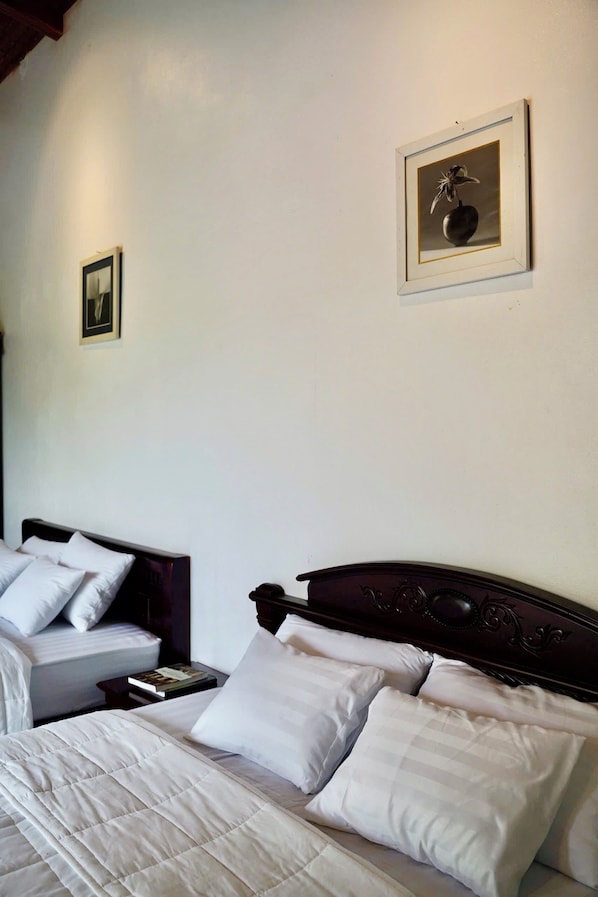 A hotel room with two beds, each with white bedding and pillows. There is a framed picture on the wall above the beds.