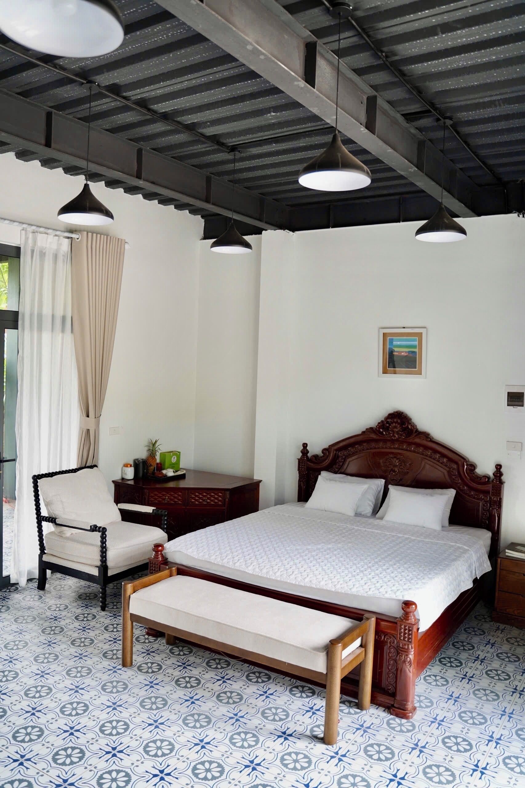 A bedroom with a bed, a chair, a bedside table, a hanging light, and a painting on the wall.