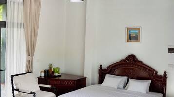 A bedroom with a bed, a chair, a bedside table, a hanging light, and a painting on the wall.