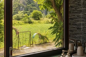 Una ventana con vistas a un jardín exuberante, un columpio y un muro de piedra.