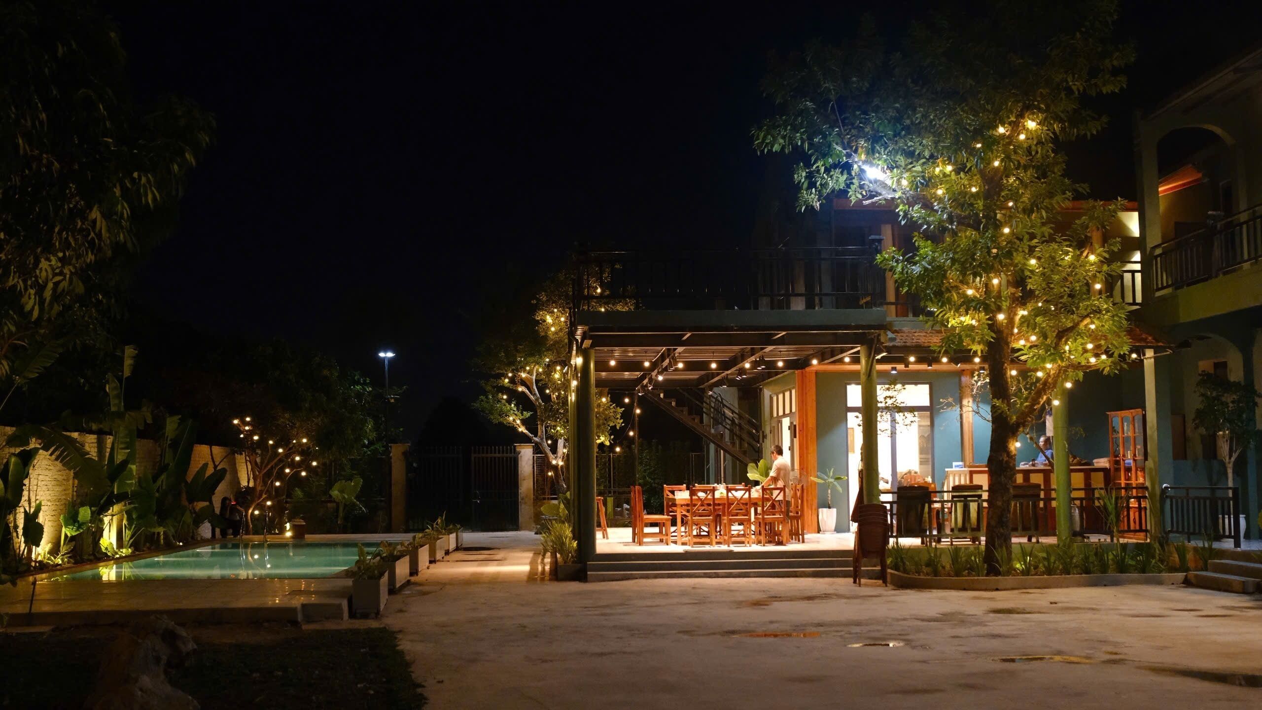 Un área de comedor al aire libre con piscina, rodeada de árboles y edificios.