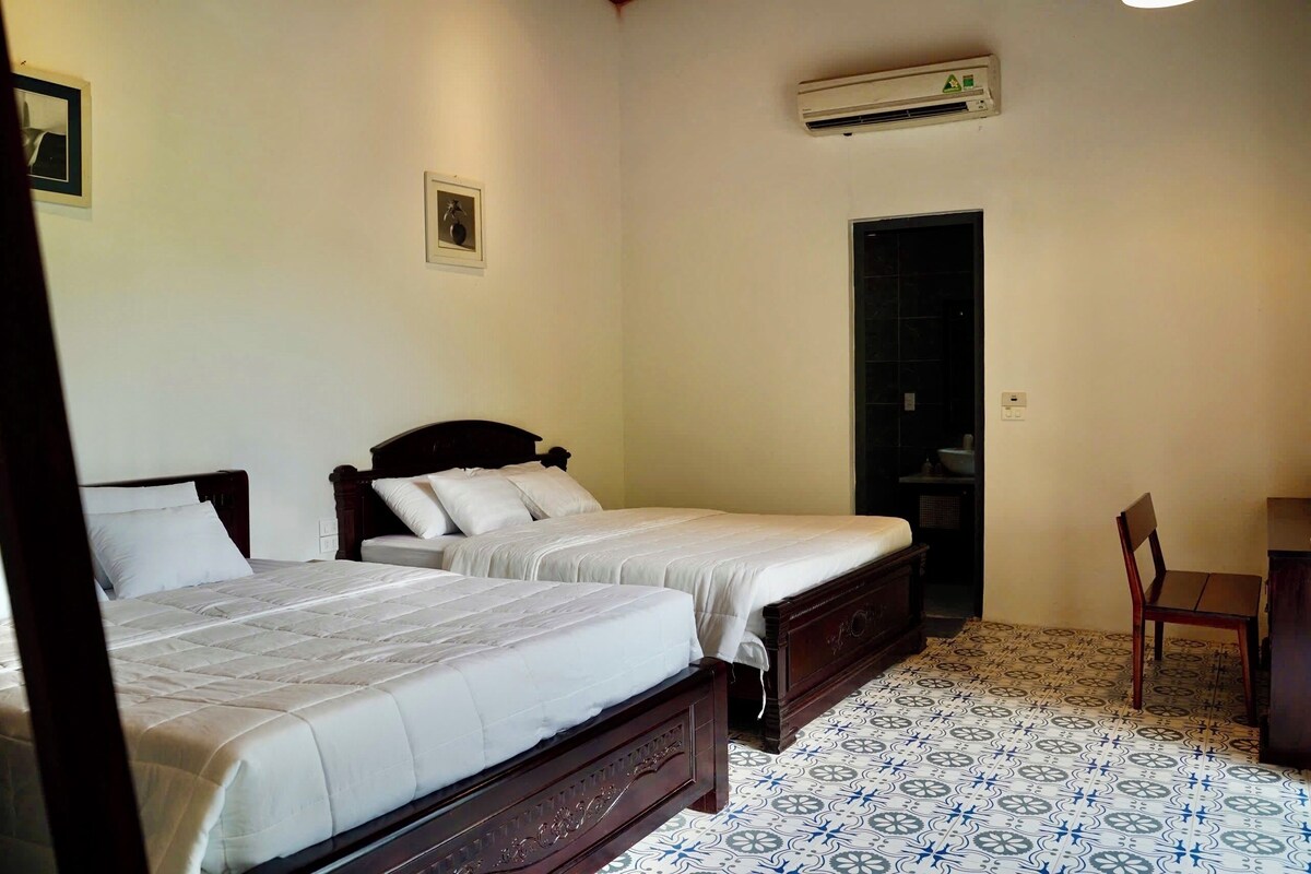 A bedroom with two beds, an air conditioning unit, a door, and a chair.