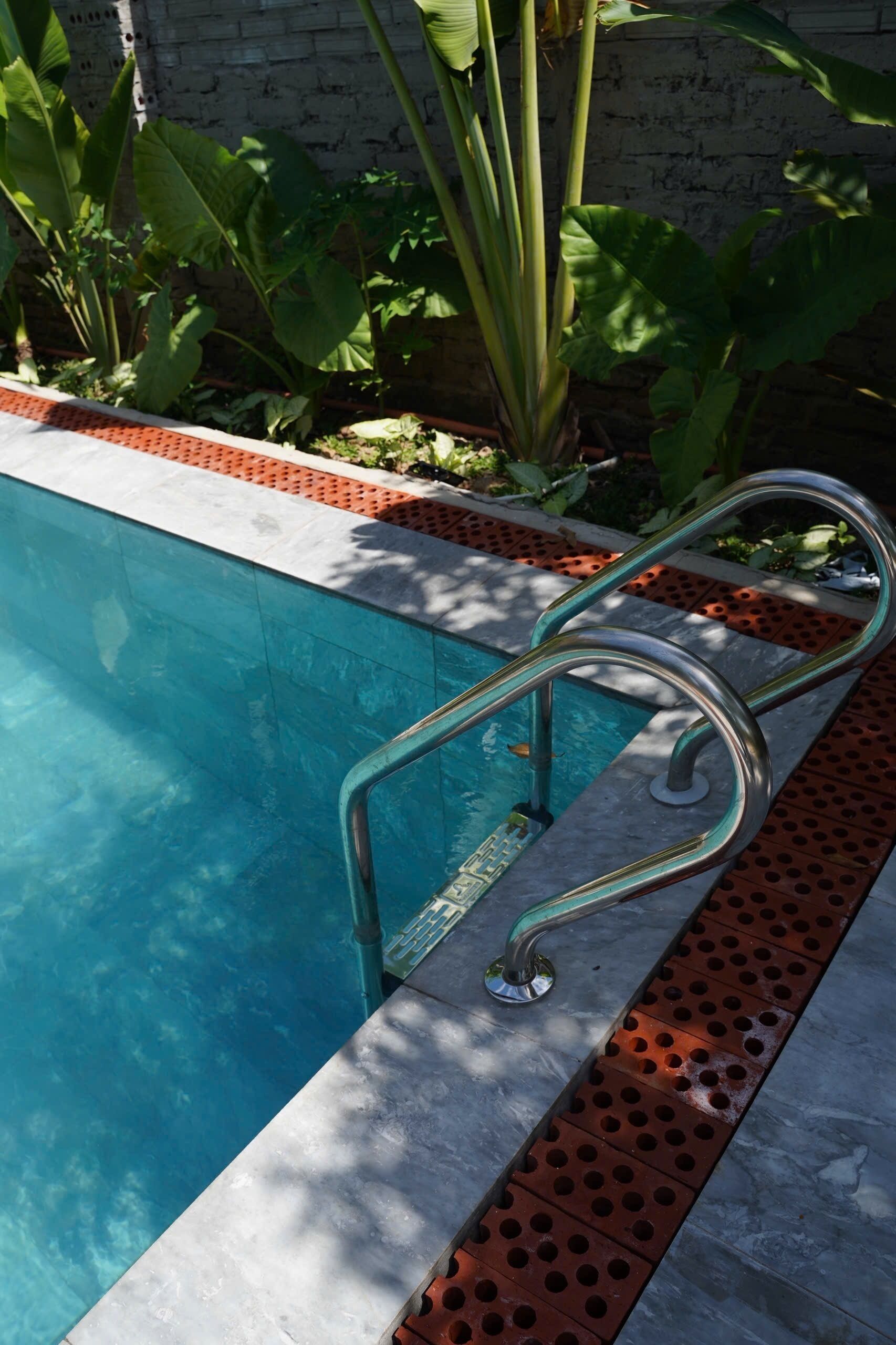 A swimming pool with a metal ladder and a red brick border.