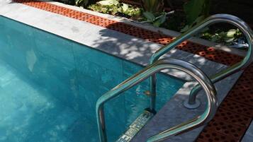 A swimming pool with a metal ladder and a red brick border.