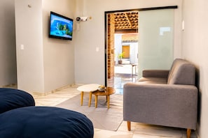 Una habitación moderna con un sofá gris, una mesita redonda y un televisor montado en la pared.