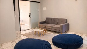 A modern living room with a grey sofa, two blue bean bags, a small white coffee table, and a glass door leading outside. - Paracuru Stay beach house with pool for families and groups of friends. (Paracuru)