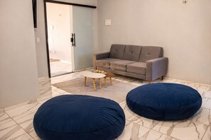 A modern living room with a grey sofa, two blue bean bags, a small white coffee table, and a glass door leading outside. - Paracuru Stay beach house with pool for families and groups of friends. (Paracuru)