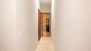 A narrow hallway with a patterned rug, wooden doors, and a shelf with items on the far end. - Paracuru Stay beach house with pool for families and groups of friends. (Paracuru)