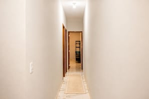 A narrow hallway with a patterned rug, wooden doors, and a shelf with items on the far end. - Paracuru Stay beach house with pool for families and groups of friends. (Paracuru)