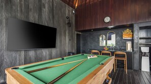 Une table de billard avec des queues, une horloge et un coin bar équipé d’un distributeur d’eau.