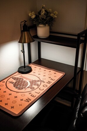 A desk with a welcome mat, a lamp, and a vase with flowers.
