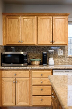 A kitchen with wooden cabinets, a microwave, a kettle, and a blender on the countertop.