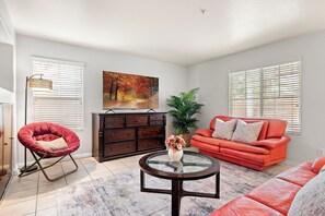 A living room with a red sofa, a red chair, a glass coffee table, a dark wooden cabinet, a painting, and a potted plant.