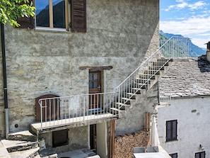 A stone building with a wooden door, a small balcony with a metal railing, and a staircase leading to an upper level.