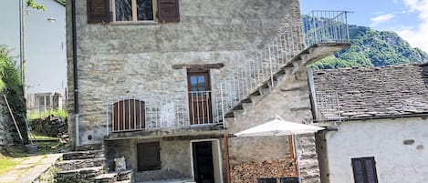 A two-story stone building with a balcony, a staircase, and a small outdoor seating area with a table and chairs.