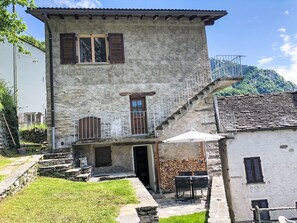 Um edifício de pedra de dois andares com varanda, escadaria e um pequeno espaço ao ar livre com mesa e cadeiras.