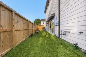A backyard with a wooden fence, a lawn, and a house with a garage. - Clean, new built spacious house, downtown, close to everything (Houston)