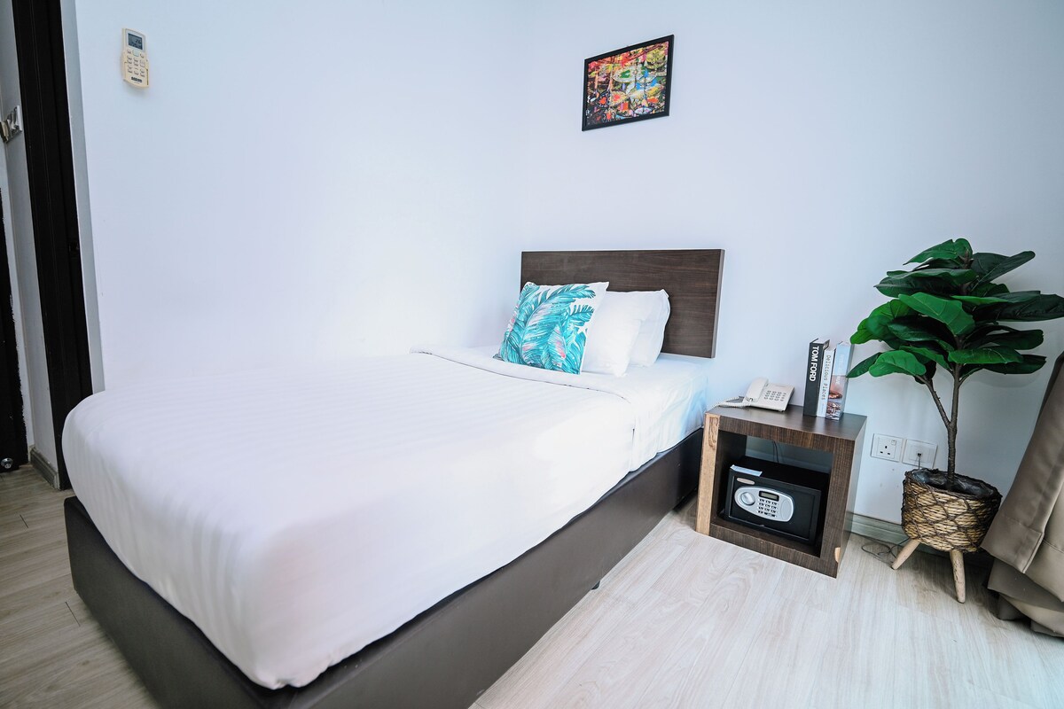 Una cama bien tendida con sábanas blancas, un cabecero y una mesita de noche con un teléfono y un libro.