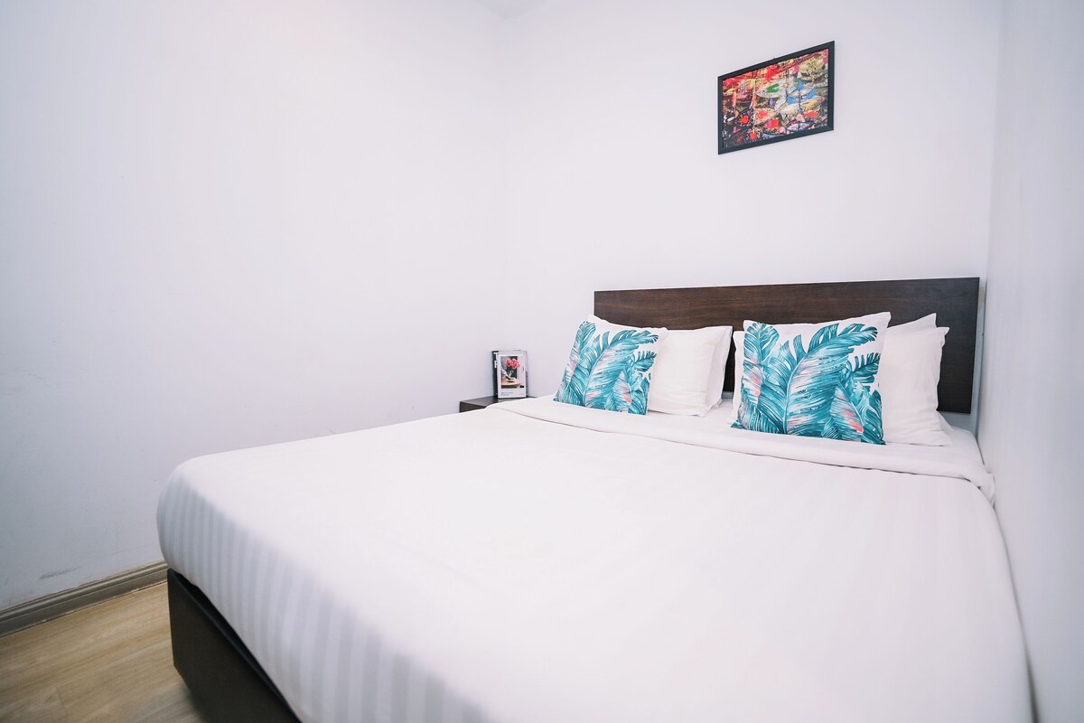 Una cama bien hecha con ropa de cama blanca y dos almohadas decorativas con diseño de hojas.