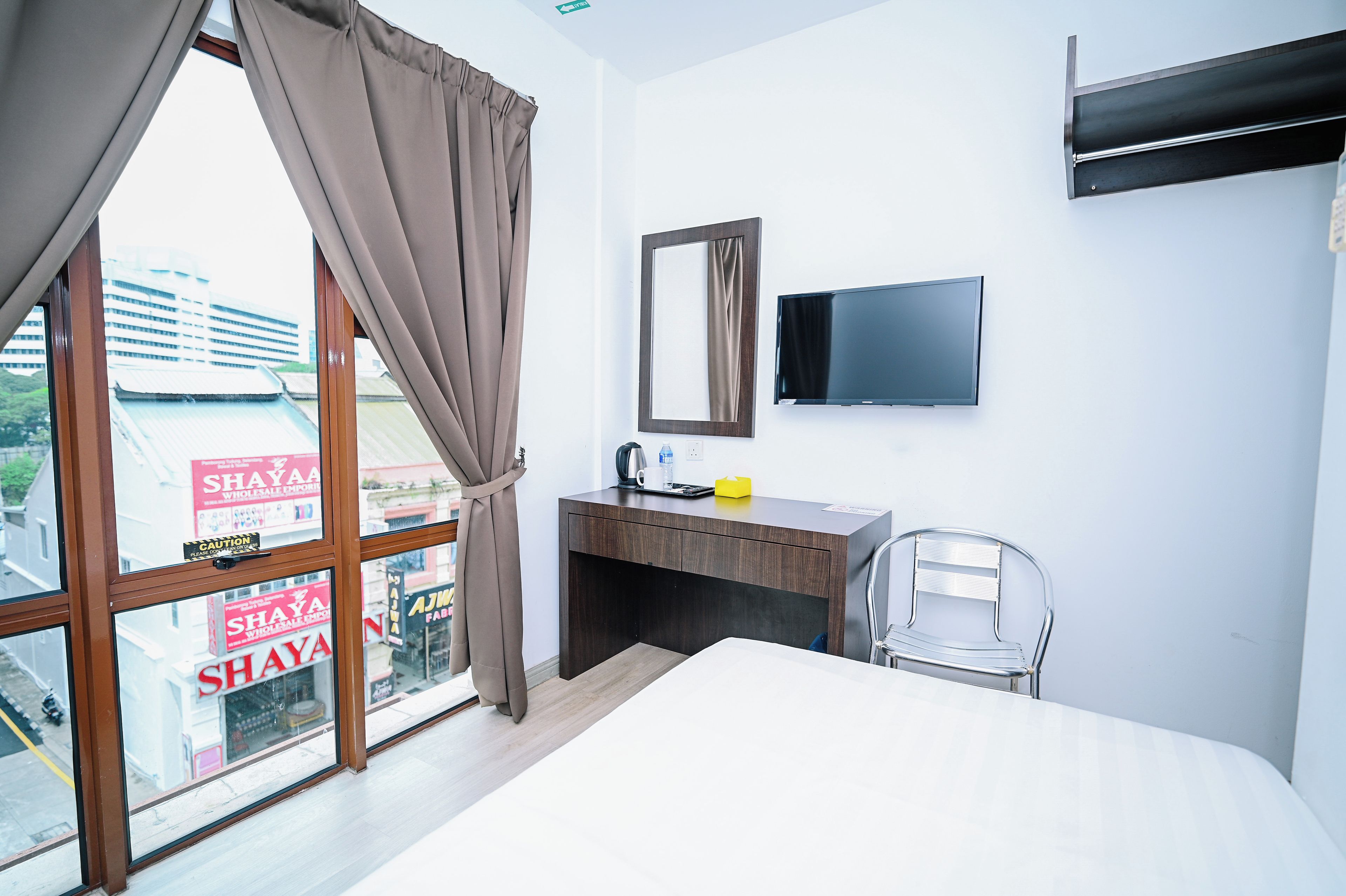 Een hotelkamer met een groot raam, een bed, een bureau met een stoel, een flatscreen televisie en een spiegel.