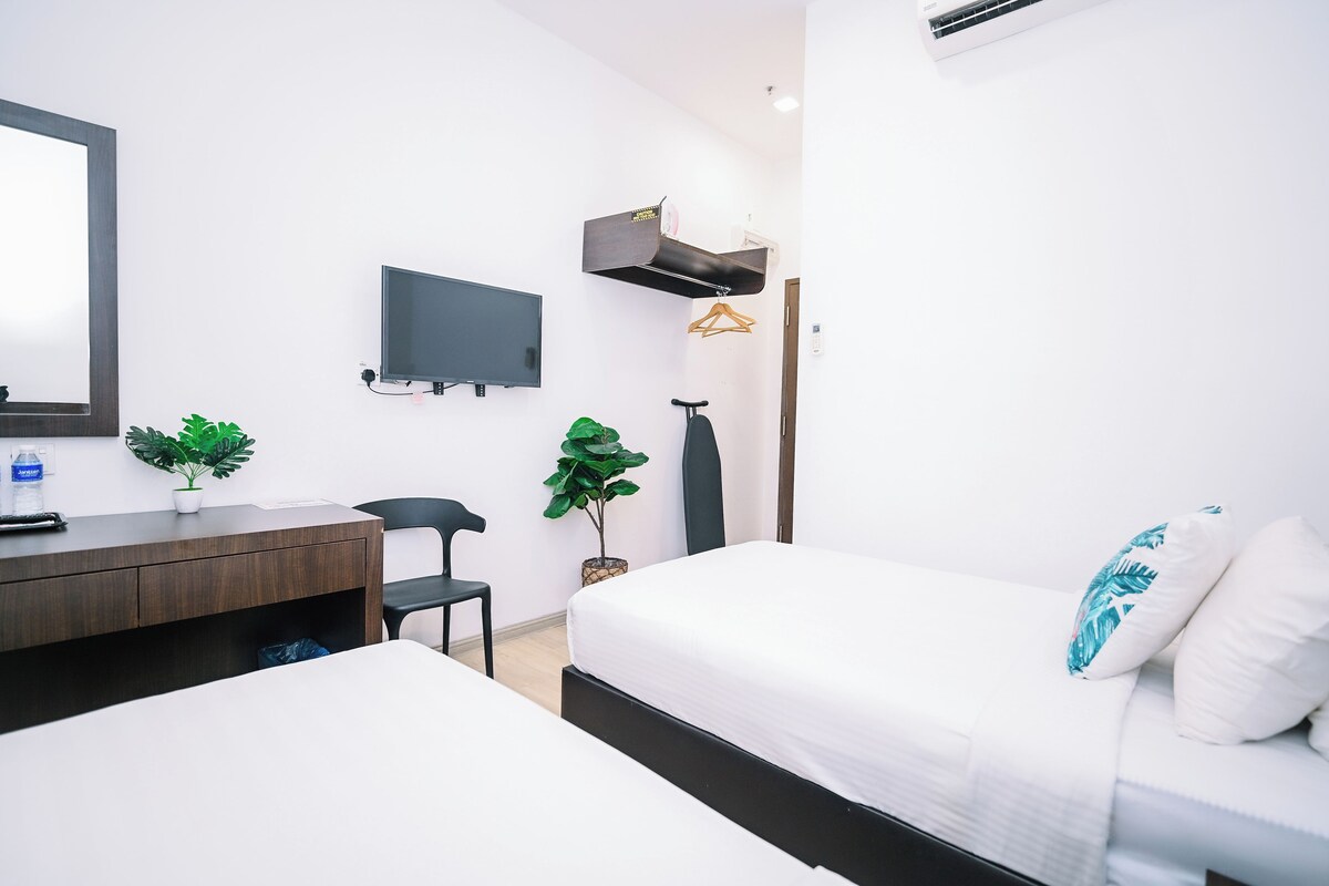 Habitación de hotel moderna con cama, escritorio, silla, televisión y lámpara colgante.