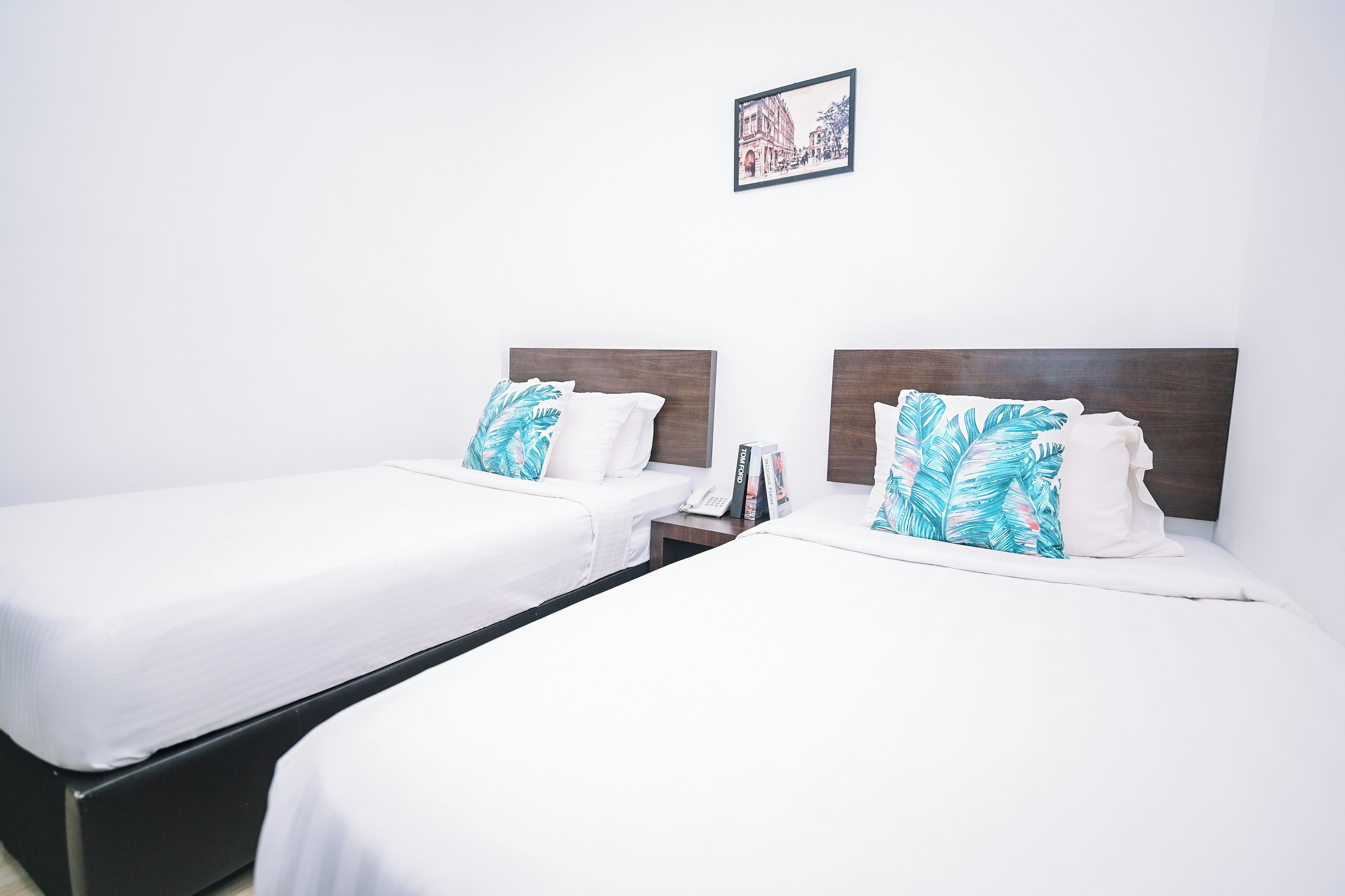 A hotel room with two single beds, each with a wooden headboard and white bedding. There is a framed picture on the wall above the beds.