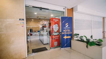 Een hotelentree met een glazen deur, een rood promotiemateriaal voor airasia ride en een blauw bord met de richting naar de hotelentree.