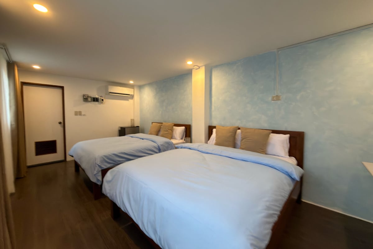 Une chambre d’hôtel avec deux lits, un plancher en bois, une porte et un climatiseur fixé au mur.
