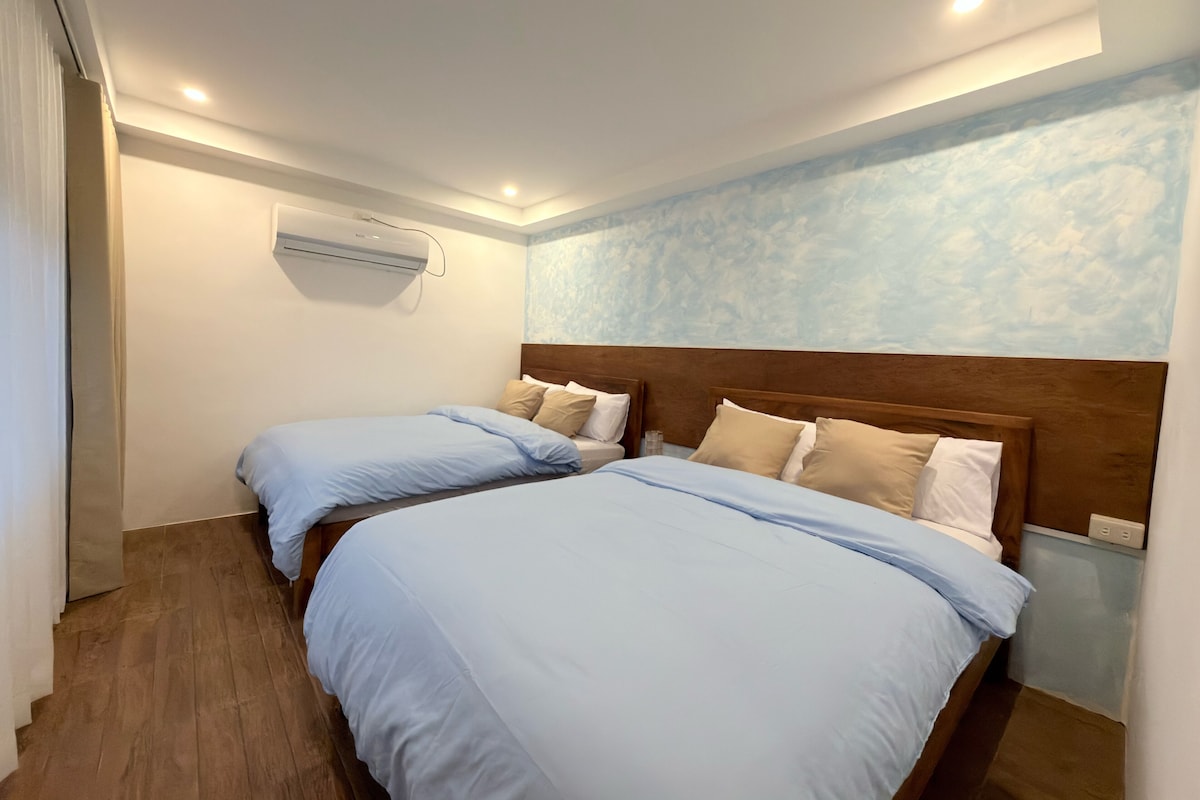 Une chambre d’hôtel avec deux lits, une tête de lit en bois, un climatiseur fixé au mur et un mur à motifs.