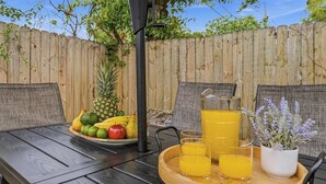 Mesa de refeições ao ar livre com um prato de frutas, uma jarra de suco de laranja e copos.