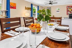 Un coin repas avec une table dressée pour quatre personnes, comprenant des assiettes, des verres et un saladier de fruits.