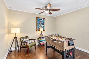 Ein Zimmer mit einem hölzernen Tischkicker, einem grünen Ledersessel, einer Stehlampe und einem Deckenventilator.