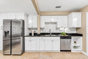 Une cuisine moderne avec des armoires blanches, des appareils en acier inoxydable et un comptoir noir.