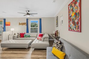 Ein Wohnzimmer mit einer Sofagarnitur, einem Deckenventilator und einem Fenster mit Vorhängen.