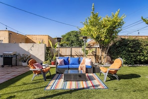 A backyard patio with a sofa set, chairs, a grill, and a striped rug. - Serene LA 2BR Retreat with BBQ & Outdoor Lounge (Los Angeles)