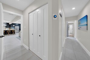 A hallway with a white door, a digital lock, and a painting of a beach scene. - Casa Solterra | 5 Bedroom Pool Retreat | Temple Terrace | Sleeps 12 (Temple Terrace)
