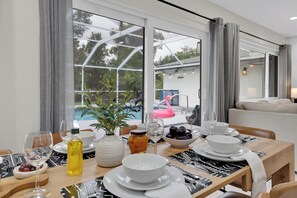 A dining table set with plates, bowls, cutlery, and glasses, with a view of a swimming pool and a flamingo outside. - Casa Solterra | 5 Bedroom Pool Retreat | Temple Terrace | Sleeps 12 (Temple Terrace)