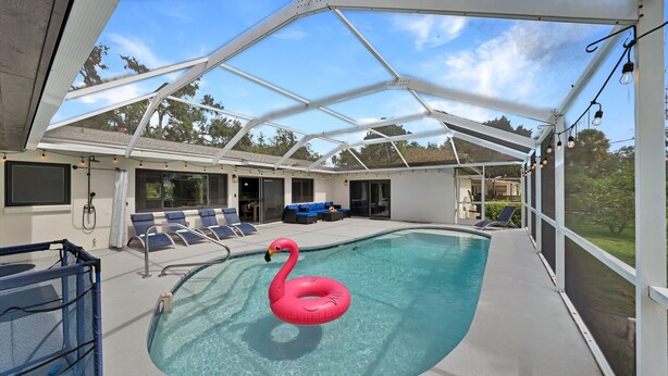 An indoor swimming pool with a pink flamingo float, lounge chairs, and a covered patio area. - Pool Days, Sunshine & Memories for Everyone (Temple Terrace)